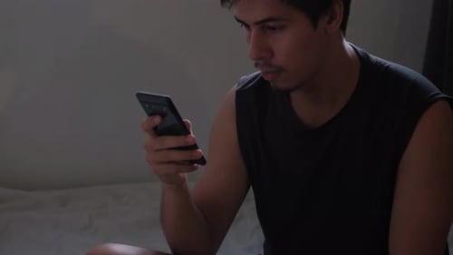 Young Adult Using Smartphone in Bedroom