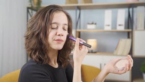 Young Woman Applies Makeup with Brush Indoors