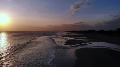 Unglaubliche Luftaufnahme eines farbenfrohen Sonnenuntergangs an einem Sandstrand, Menschen, die am Strand spielen — fliegen
