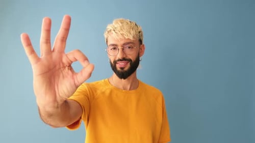 Close up, man showing ok gesture, looking at camera isolated on blue background in studio