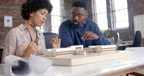 Focused diverse architect colleagues discussing work with building model in office in slow motion