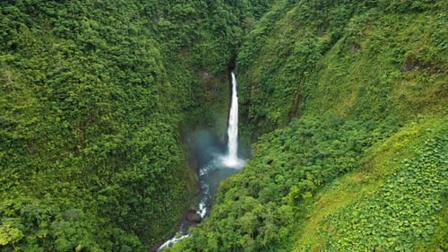 Tall rainforest waterfall surrounded by lush green cliffs and mist in Costa Rica
