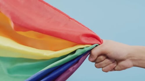 Hand Holding Rainbow Flag Against Blue Background