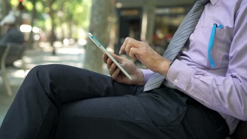 Businessman browsing on tablet computer sitting on bench in the city