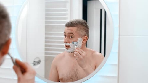 Man Shaving His Face in Bathroom Mirror