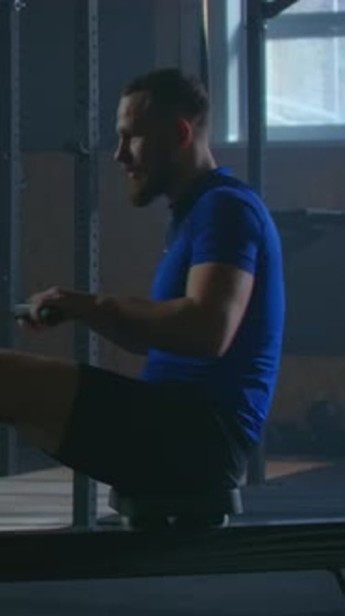Focused Athlete Training on Rowing Machine in Dimly Lit Gym Demonstrating Strength Endurance and