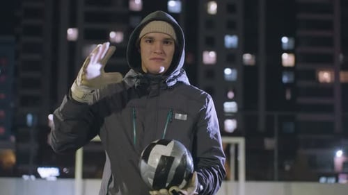 Man in Hoodie Hitting Soccer Ball on Urban Sports Field at Night