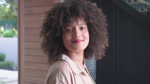 African American woman near sliding glass doors, turning toward approaching camera and smiling