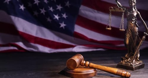 Judge's gavel and statue of Lady Justice on wooden table against flag of USA, closeup