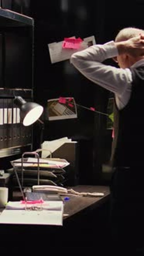 Man Inspecting Documents at Desk in Dark Office