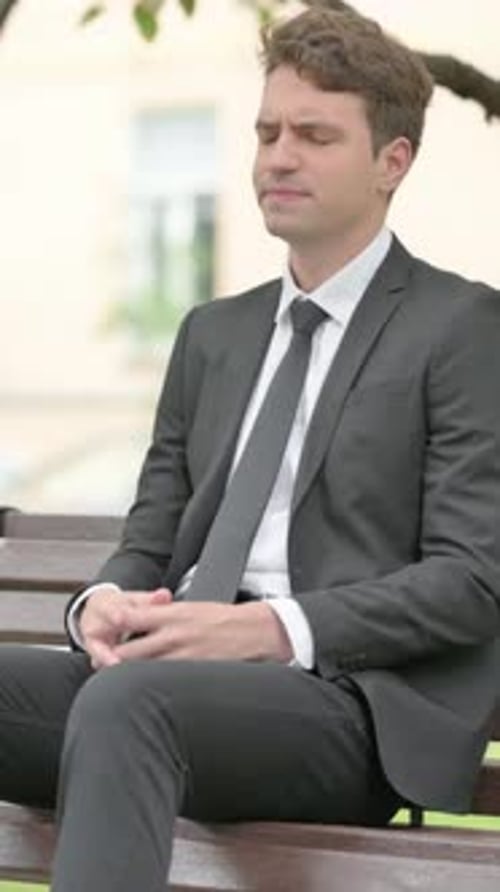 Man in Suit with Headache Sitting on Bench