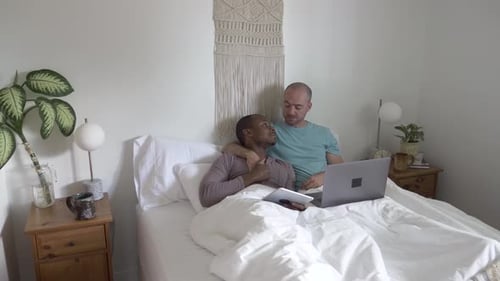 Two men in bed looking at technology