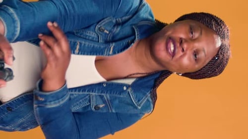 Woman Speaking Holding Tripod Against Orange Background