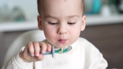 Adorable Toddler Eats Food With Spoon at Home