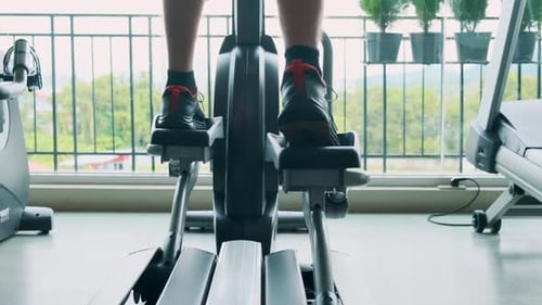 Man Exercising on an Elliptical Trainer in Modern Gym with Close Up on Legs and Pedals Male Doing