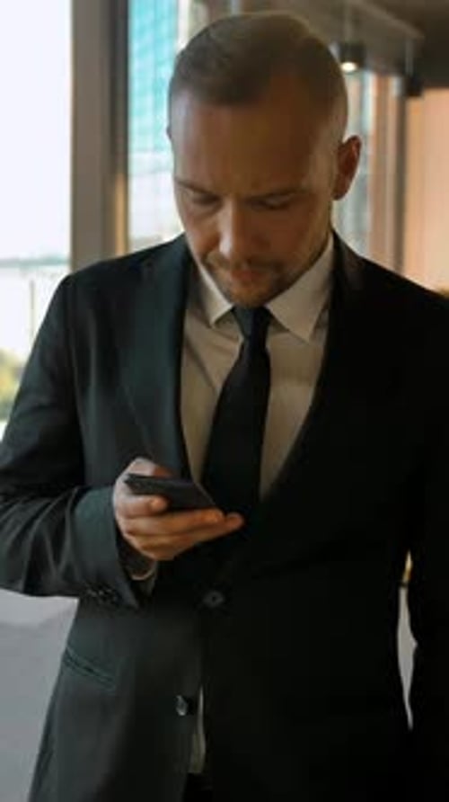 Vertical of Portrait of a Handsome Man Standing Near Window in Loft Room and Writing Sms