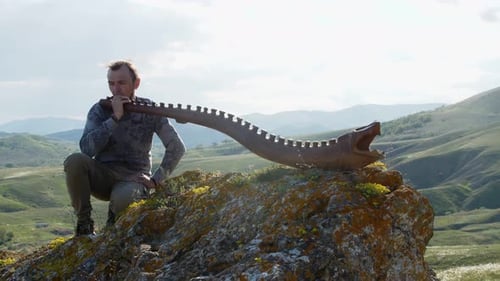 A Musician Daydreams with an Australian Aboriginal Musical Instrument Didgeridoo on a Rock Ledge on