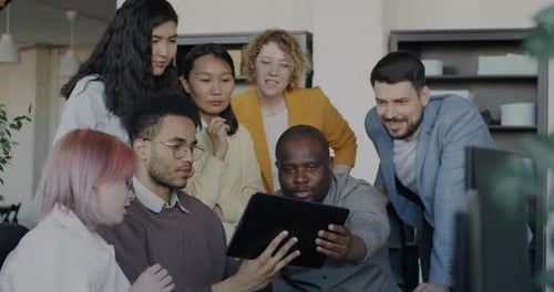 Diverse Business Team Talking and Looking at Tablet Screen Discussing Work in Office