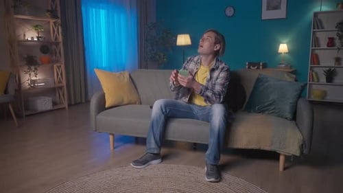 A Man Sits on the Couch Turns on the TV with the Remote Control A Man Adjusts the Brightness of the
