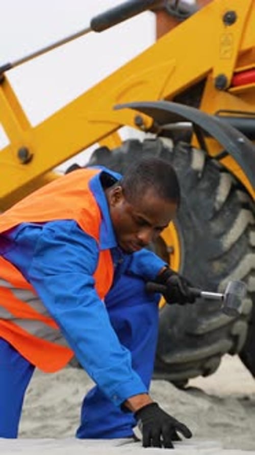 African American Construction Worker Laying Paving Stones Near Excavator