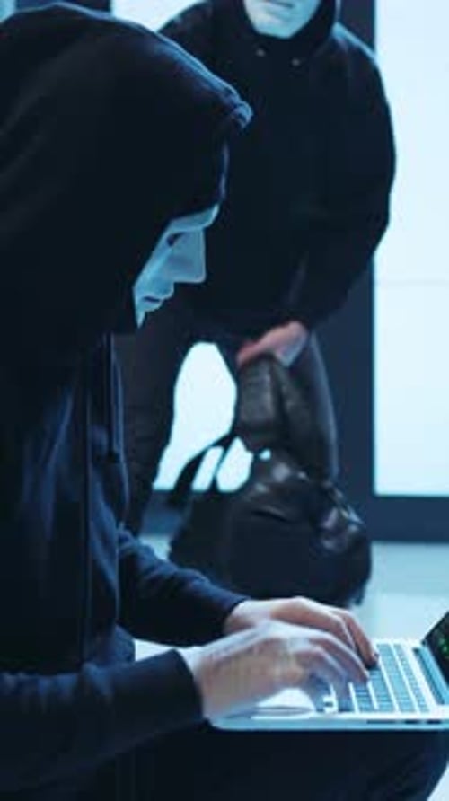 A Mysterious Hacker Dressed in a Masking Hood is Intently Working on a Laptop Device