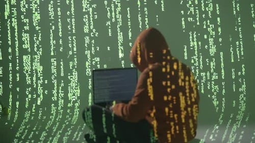 Masked Hacker in Hoodie Surrounded by Green Matrix Code Working on Laptop