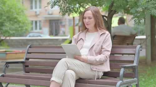 Woman Using Tablet on Bench Celebrates Success