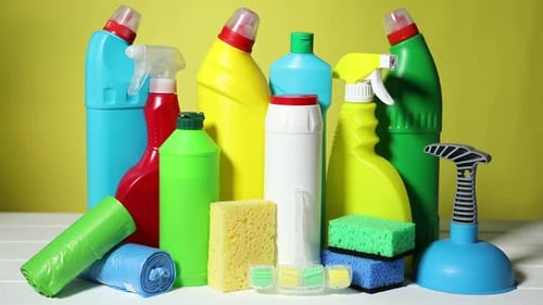 Woman with toilet cleaning products and supplies at white table against yellow background, closeup
