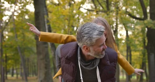 Grandfather Holding Granddaughter Piggyback in Autumn Park