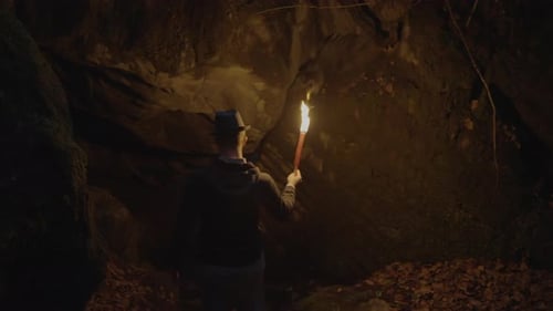 Man Holding A Burning Torchlight Exploring Forest Cave Landscape In Dark Night
