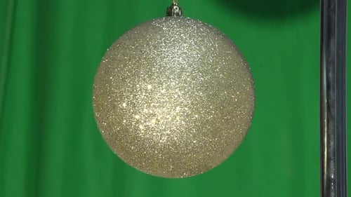 This video shows a gold glitter Christmas ornament ball hanging by a string and slowly spinning arou