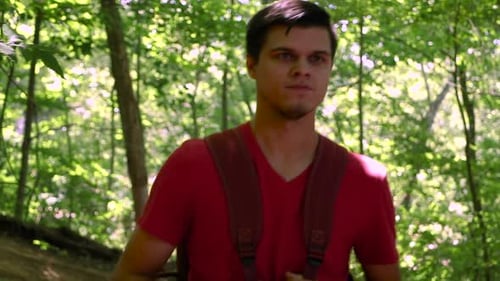 Young millennial guy with backpack hiking through the woods