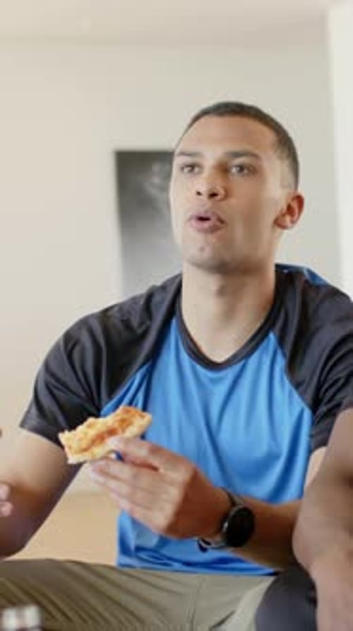 Vertical video: Reacting to friend's gesture, man sitting up in blue shirt on couch, holding pizza