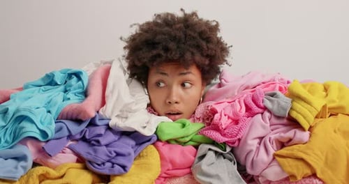 Unhappy African American Woman Drowned In Multicolored Laundry Looks Away Feels Frustrated And Ti...