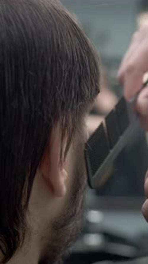 In einem Friseurladen schneidet ein männlicher Stylist die Haare eines jungen brünetten Mannes mit einem Kamm sauber ab und