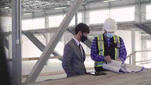 Architect and foreman reviewing blueprints in empty warehouse development
