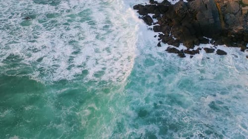 Schaumige Wellen, tonnenförmige Felsen, Nahaufnahme, plätscherndes Surfwasser, das schwarze Klippen bedeckt