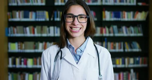 Una joven y hermosa doctora en una biblioteca sonriendo feliz y sosteniendo libros después de hacer un mar