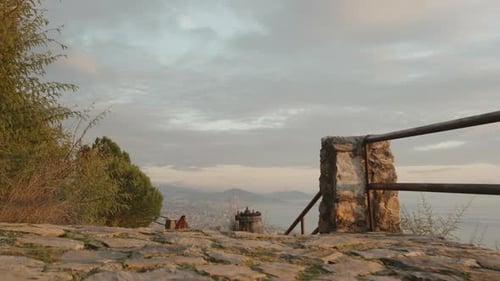 A rocky path descends from the mountain with railings leading to the city. In the distance.