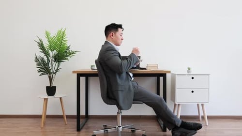 Asian Businessman Relaxing with Coffee in Modern Office Setting