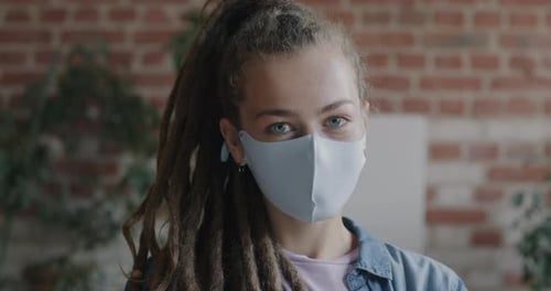 Portrait of Young Lady with Dreadlocks Wearing Facial Mask Looking at Camera in Loft Style Office