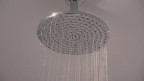 Foto estática de um chuveiro redondo prateado do qual a água flui em um banheiro moderno