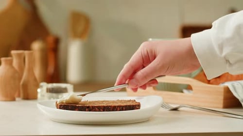 Hand Spreads Cream on Bread in Kitchen