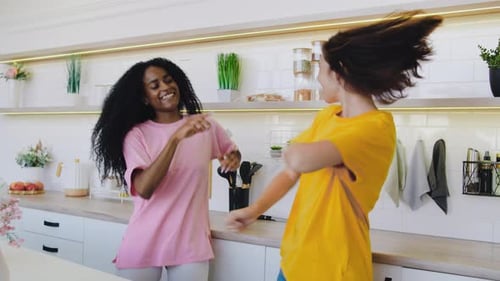 Two Young Women Dancing Joyfully in Modern Kitchen
