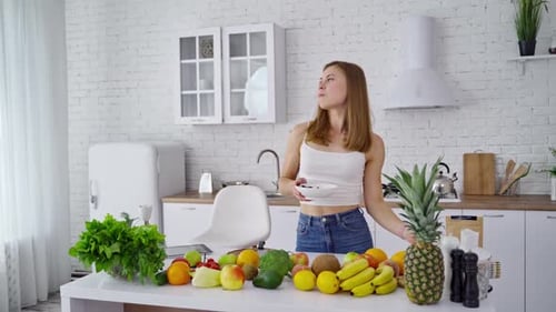 Woman Eating Fruit in Bright Kitchen