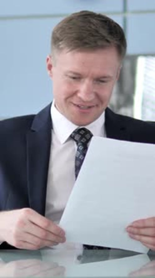 Excited Businessman Reading Document at Desk in Office