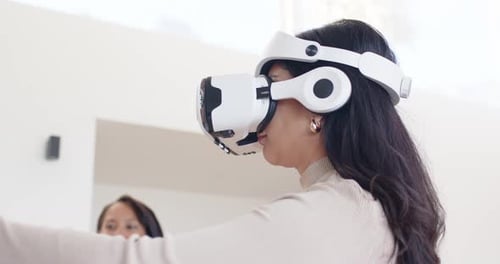 Dupla feminina na sala de demonstração, usuário de realidade virtual atendendo às instruções do aplicativo, estendendo as mãos como observadora verificando o tablet