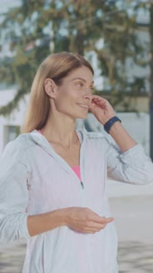 Woman Puts Wireless Earbud in Her Ear Outdoors