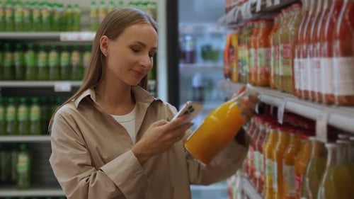 Woman Choosing Fresh Juice at Supermarket Using Smartphone for Scanning Barcode