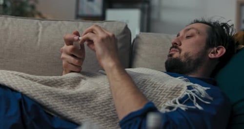 Un homme à la barbe est allongé sur un canapé et recouvert d'une couverture